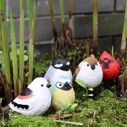 A collection of colorful painted bird figurines, including a Northern Cardinal, surrounded by greenery.