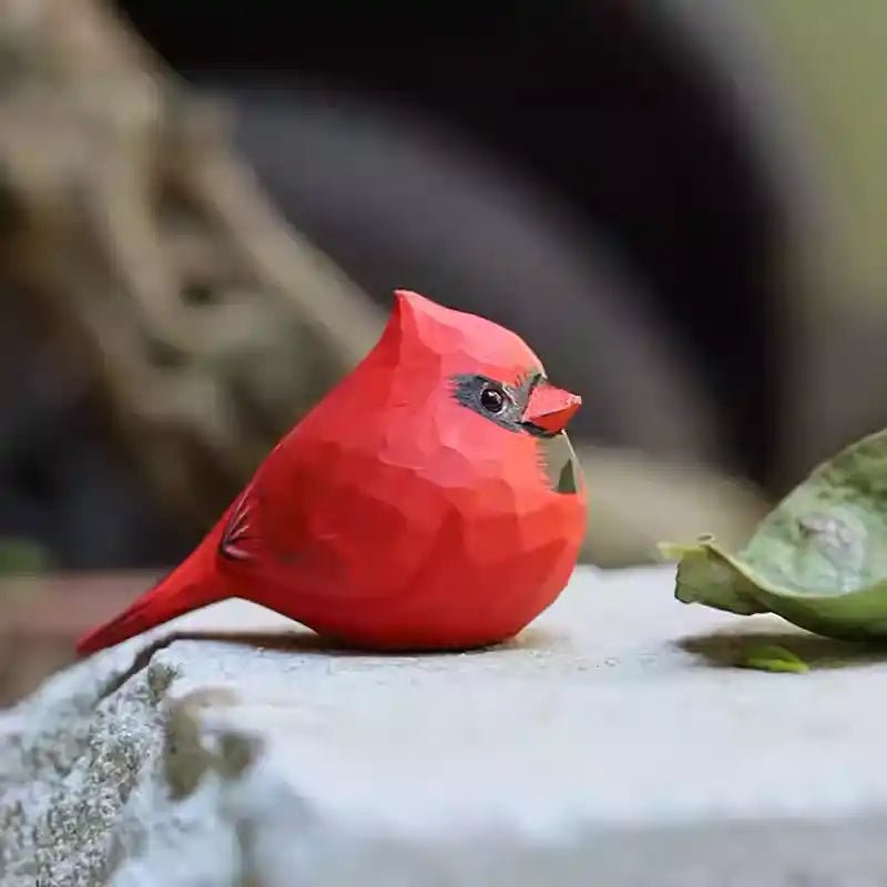 A decorative red bird figurine sitting on a stone surface, surrounded by leaves.