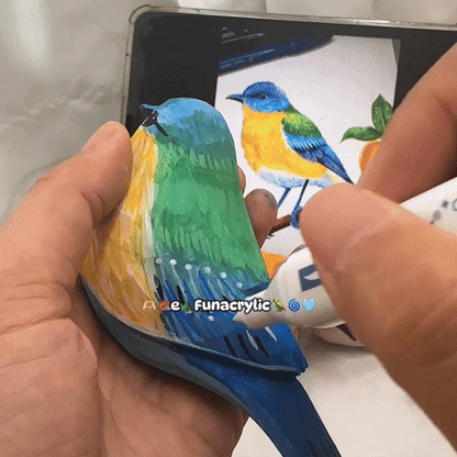 A person painting a colorful wooden bird using markers alongside a reference image.
