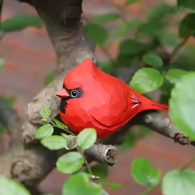 A detailed red cardinal bird resting on a branch surrounded by green leaves.