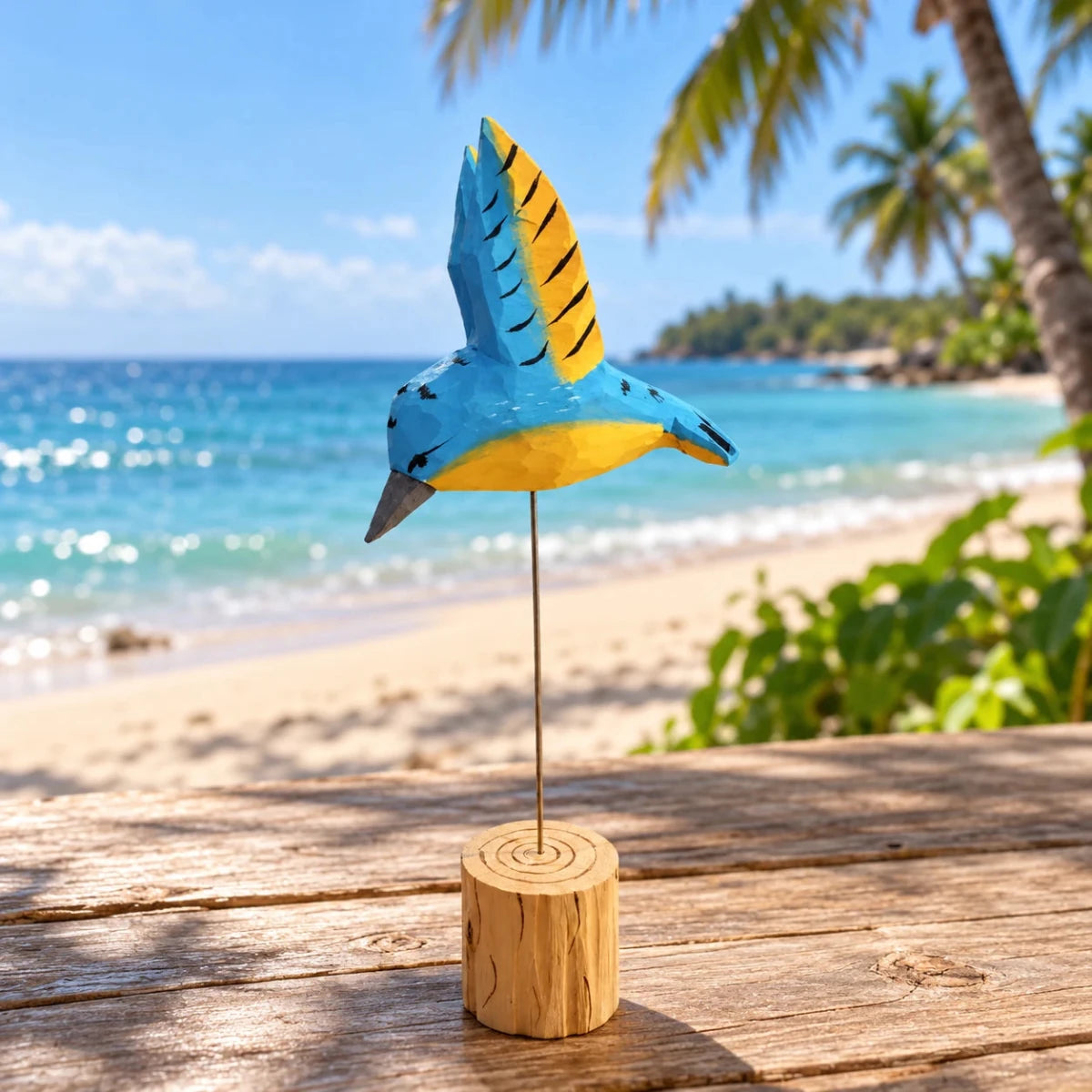 Blue and yellow hand-painted wooden hummingbird ornament on a wire stand at a tropical beach