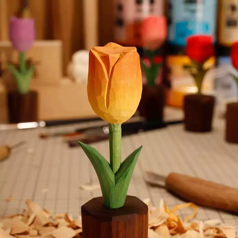 A vibrant, handcrafted wooden tulip with an orange and yellow gradient, standing in a dark wooden base, surrounded by artistic tools and colorful background.