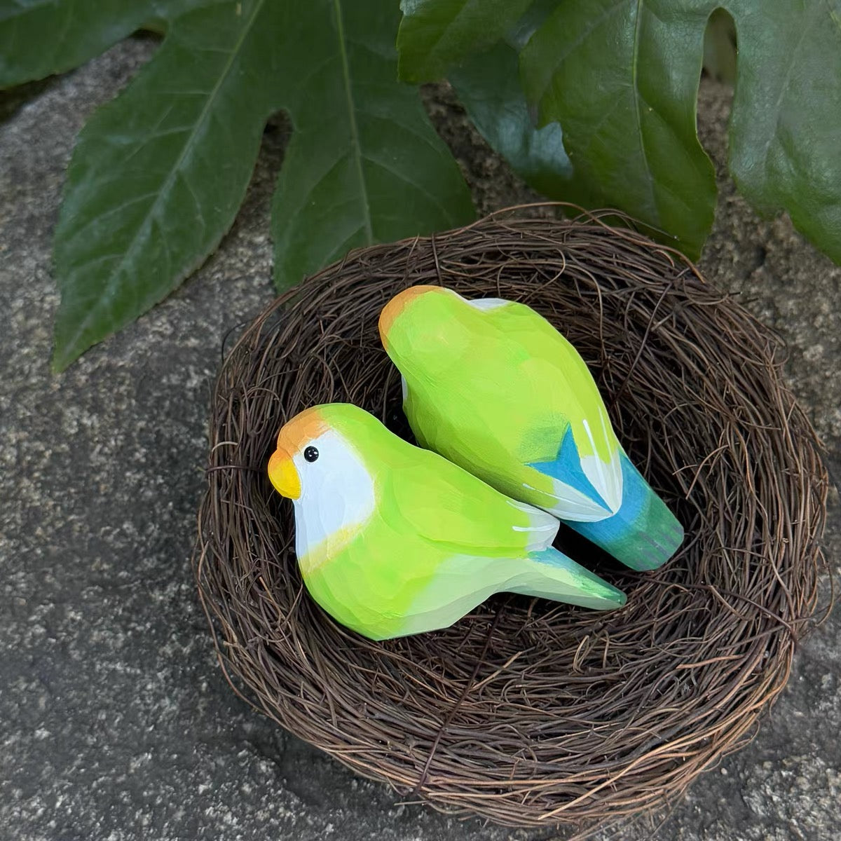 Pair of green hand-painted wooden parrots in a bird nest