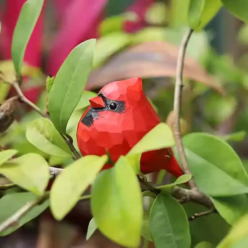A detailed red cardinal bird resting on a branch surrounded by green leaves.