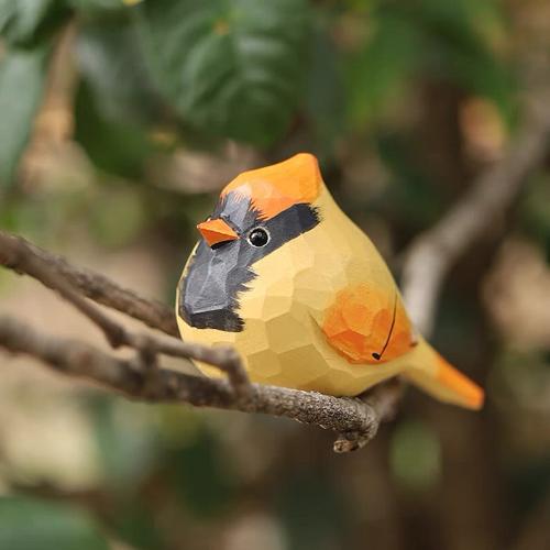 Close-up of a hand-painted wooden goldfinch figurine resting on a tree branch, showcasing vibrant colors and natural basswood texture