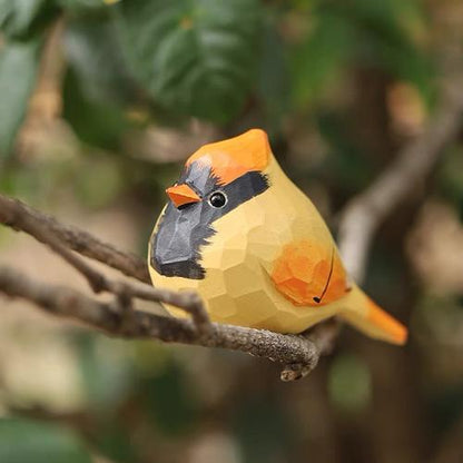 Close-up of a hand-painted wooden goldfinch figurine resting on a tree branch, showcasing vibrant colors and natural basswood texture