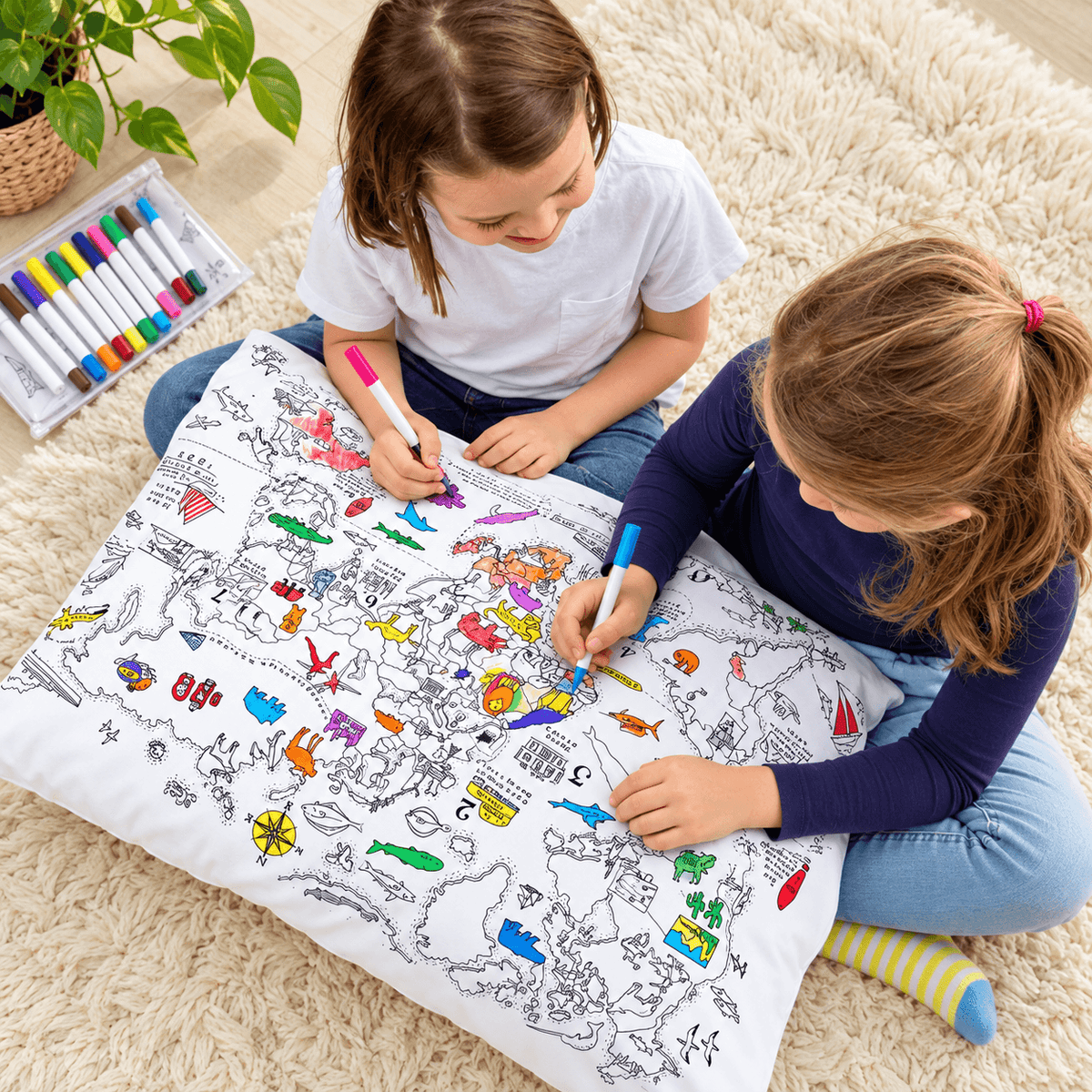 Two girls coloring a detailed world map pillowcase together with fabric markers