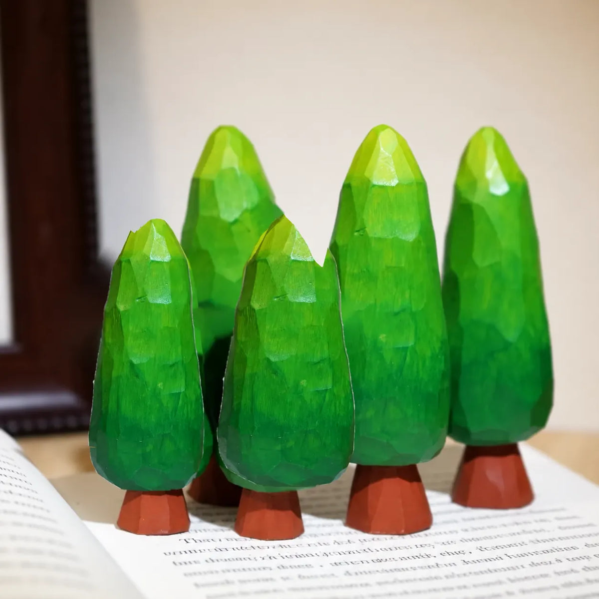 Green painted wooden trees displayed together on an open English book