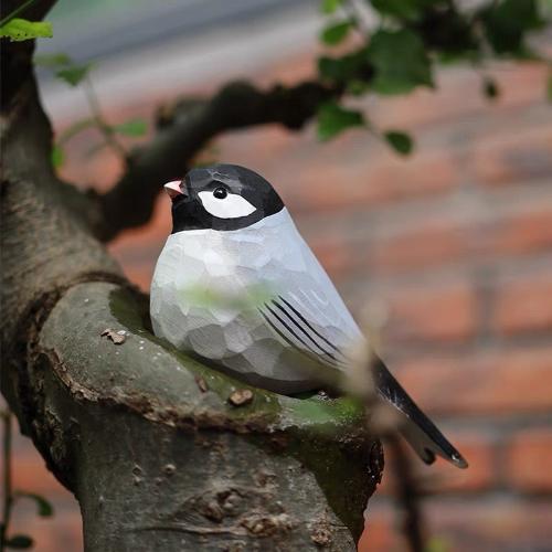 A gray wooden painted swallow perches on a tree branch