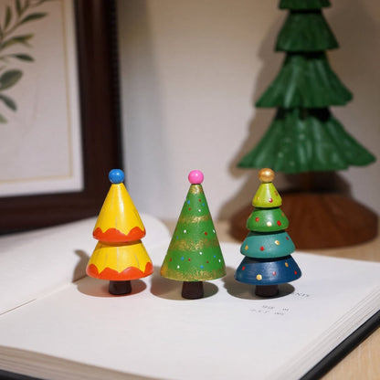 Three hand-painted wooden Christmas trees displayed on a book for festive holiday decor.