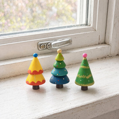 Three hand-painted wooden Christmas trees displayed on a bright windowsill for holiday decor.