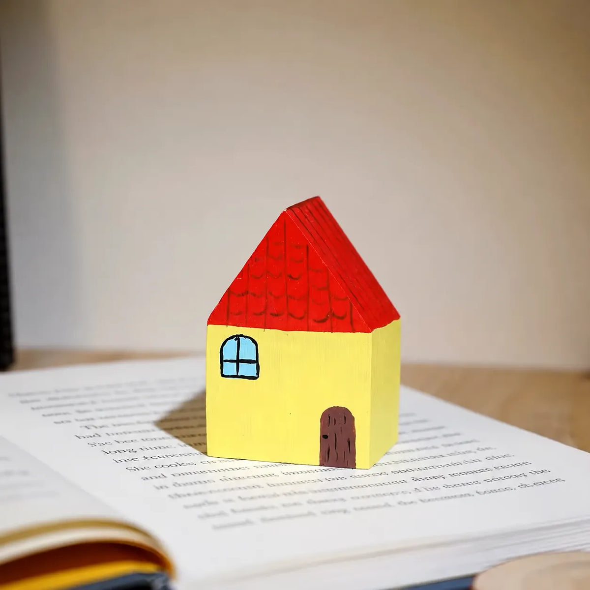 Yellow and red painted wooden house displayed on an open English book