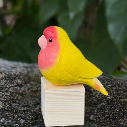 Red and yellow hand-painted wooden parrot displayed on a wooden block