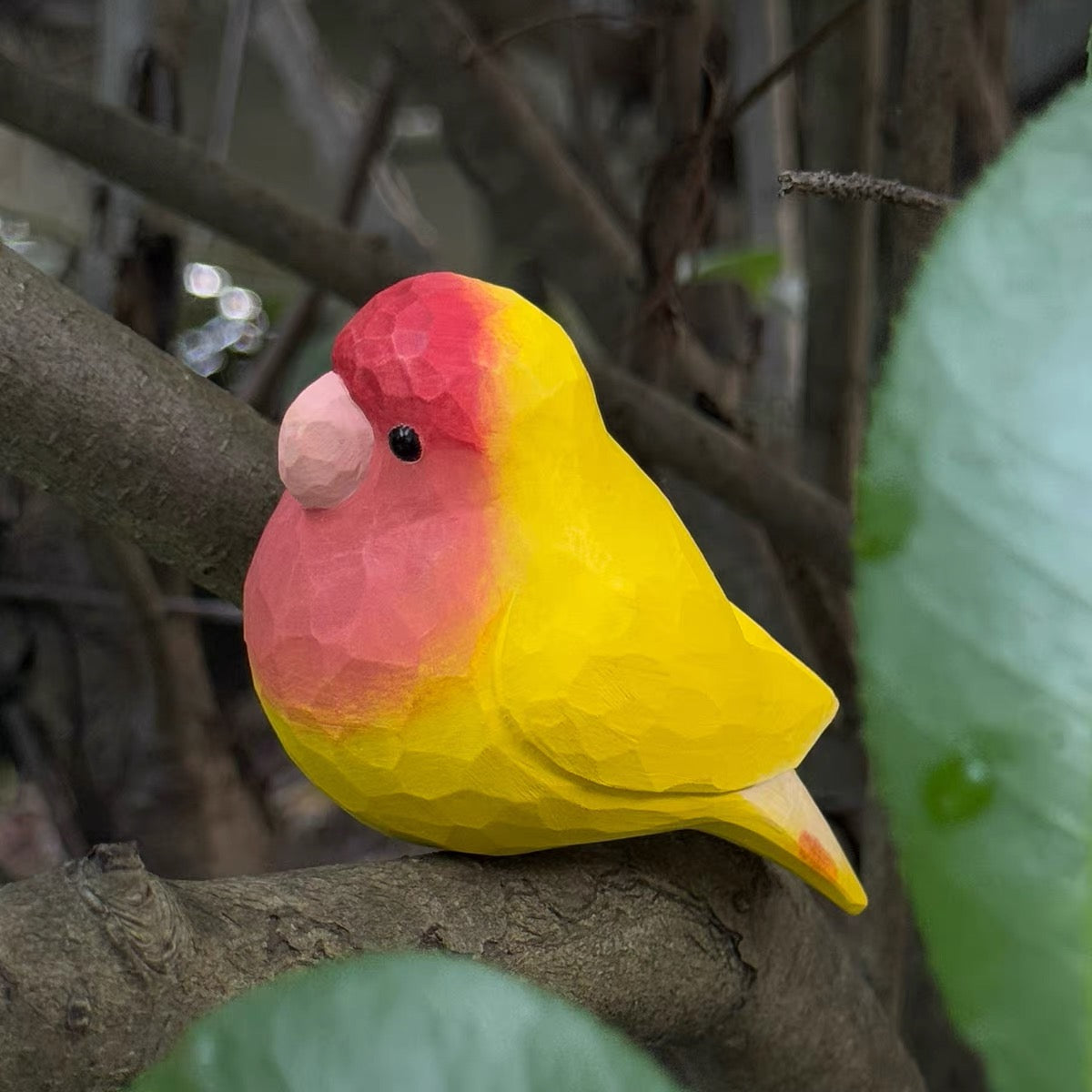 Red and yellow hand-painted wooden parrot sitting on a branch
