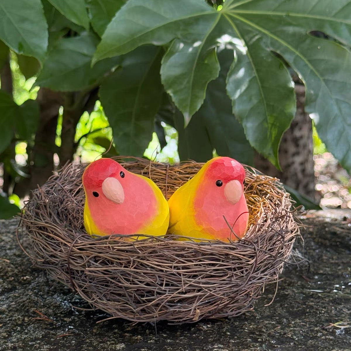 Pair of red and yellow hand-painted wooden parrots in a bird nest