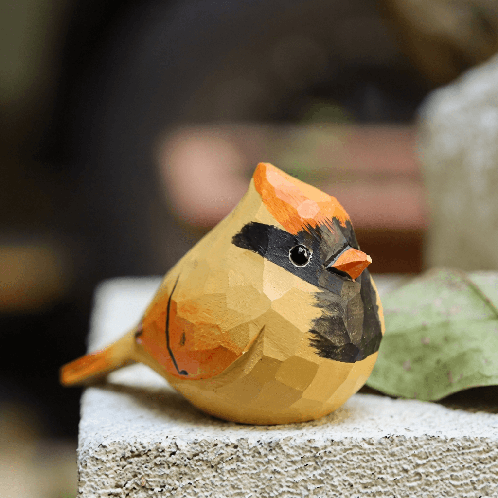 A colorful, geometric bird figurine sitting on a stone surface with a leaf nearby.