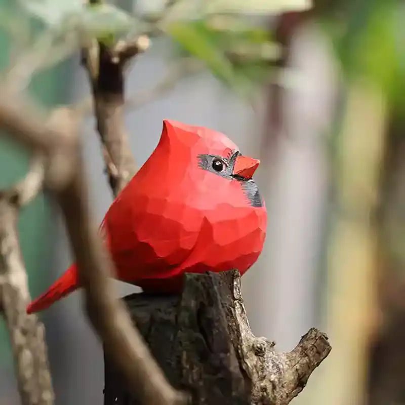 A vibrant, geometric red cardinal bird sculpture perched on a branch, surrounded by greenery.