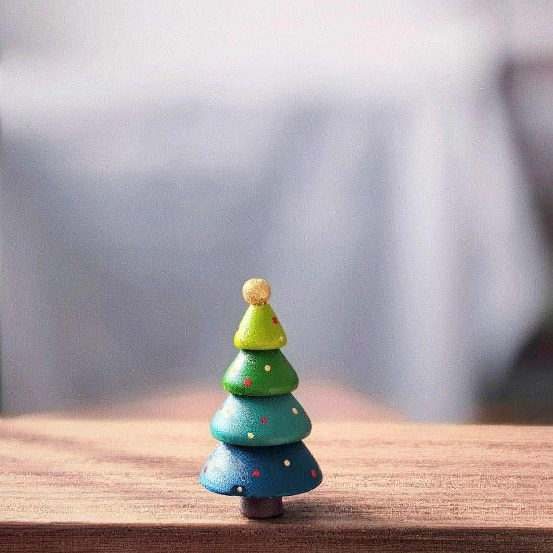 Colorful stacked wooden Christmas tree painted in rainbow colors with a gold bead topper.