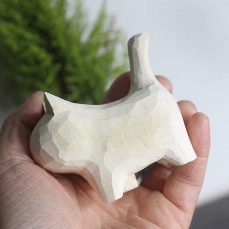 A person's hand holding a unique wooden cat figurine crafted with a geometric design.