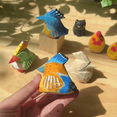 Hands painting colorful details on a wooden hoopoe bird figurine