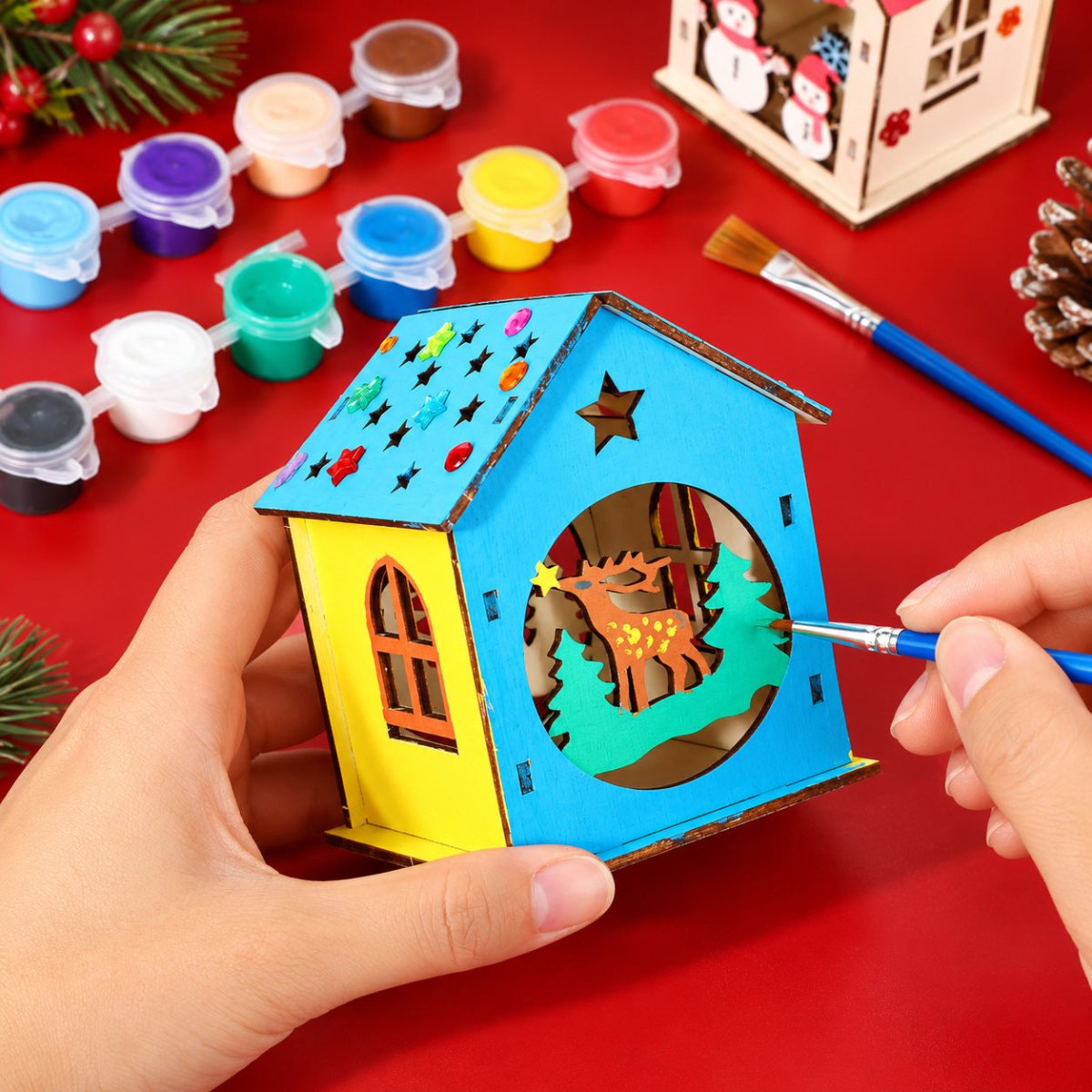 Hand painting a wooden reindeer Christmas house with a small brush