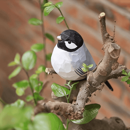 A wooden swallow bird bird figure perched on a branch surrounded by green leaves.
