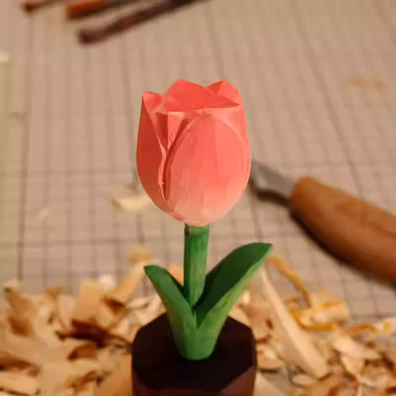 A handcrafted pink wooden tulip sculpture with green leaves, placed on a workbench surrounded by wood shavings.